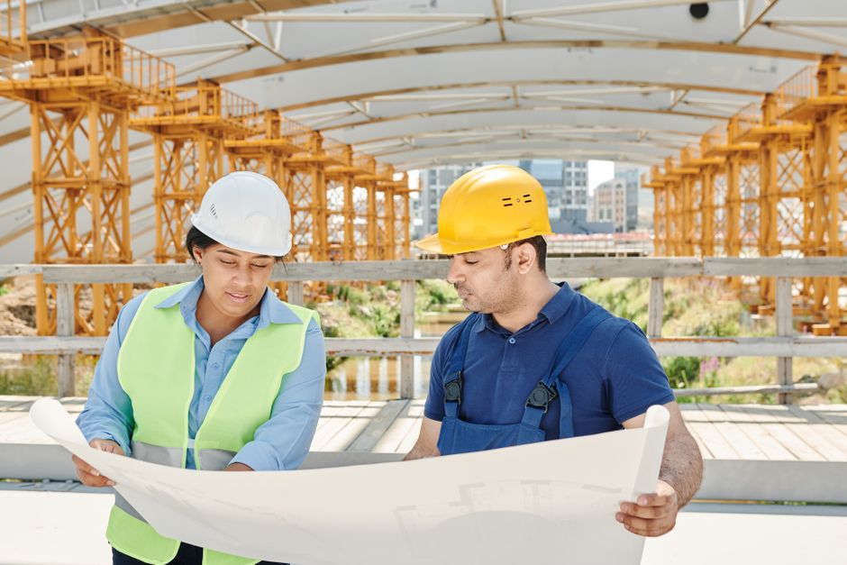 Un technicien, des plans et un chantier en extérieur